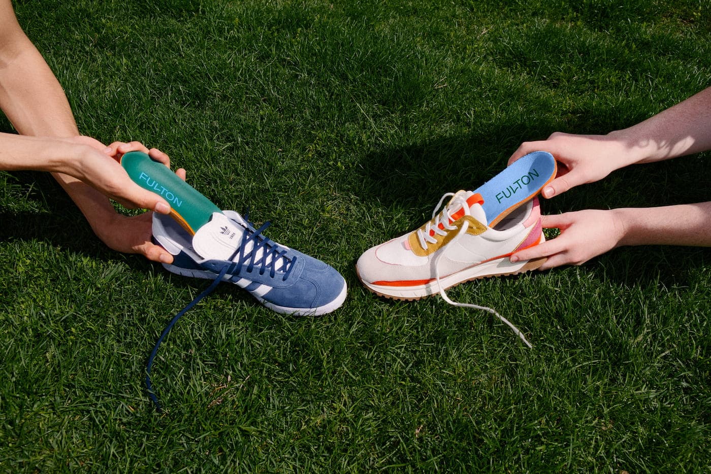 Two people lying in grass holding Fulton orthopedic insoles next to their sneakers